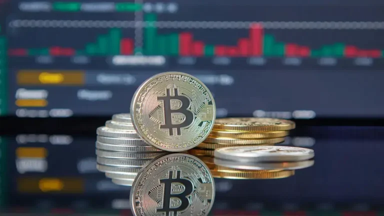 Bitcoin podría llegar a 170000: monedas físicas de la criptomoneda sobre una superficie reflectante con un gráfico bursátil de fondo que muestra la tendencia alcista del mercado.
