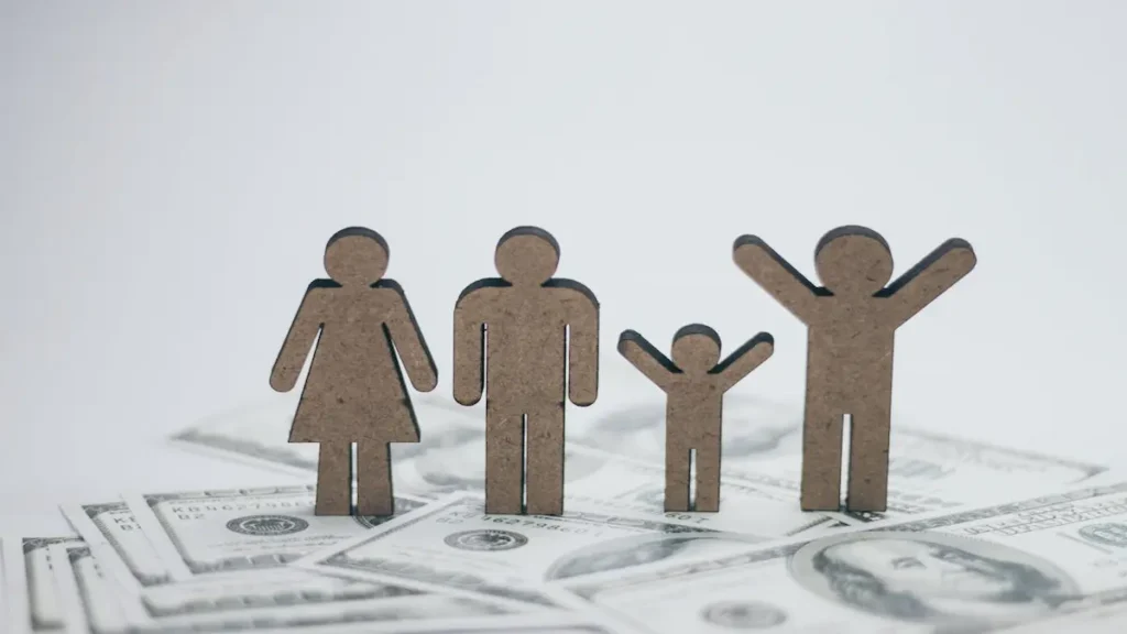 Figuras de madera que representan una familia sobre billetes de dólar para aprender a crear un presupuesto familiar desde cero.