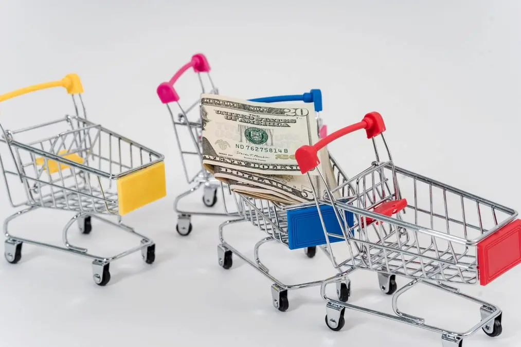 Carritos de compra en miniatura junto a billetes de dólar para representar el impacto de la inflación en el consumo.