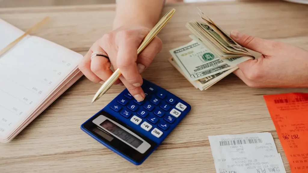 Persona usando una calculadora y contando billetes de dólares para crear un presupuesto familiar efectivo.
